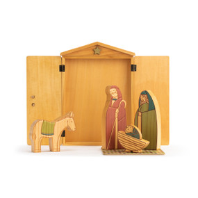 A wooden Journey to Bethlehem Nativity Set. A wooden shed placed behind small wooden figures of baby Jesus in a manger, Joseph, Mary, and a donkey.