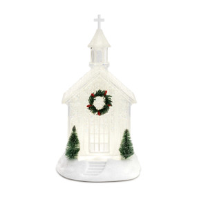 An illuminated crystal figure of a church with a green and red wreath, and two Christmas trees on each side.