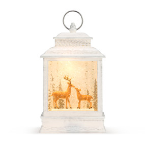 An illuminated white washed wooden musical lantern, with a two deer, Christmas trees, and faux snow enclosed. With a silver ring.
