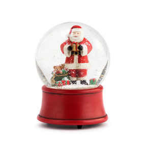 A red snowglobe enclosing faux snow and Santa holding a gold and red present beside a large green sack filled with presents.