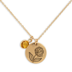 Detail view of the charms on a delicate gold necklace with a round gold charm with the birth flower for November and a separate birthstone.