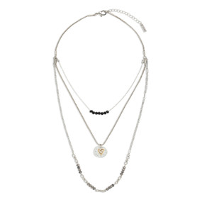 A silver three strand necklace with black beads and a charm that is a mixed metal circle with a gold heart.