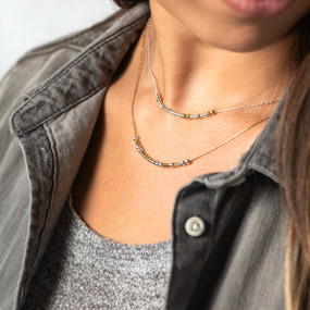 Close up of a woman wearing a gold and silver two strand necklace with beads and bars representing a morse code message.
