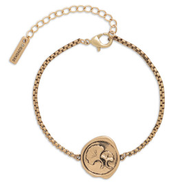 A gold metal bracelet that has a round metal charm with two leaves.