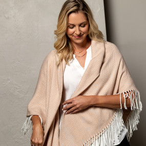 A woman wearing a camel and cream striped fringed blanket wrap in front of a gray background.
