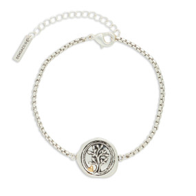 A silver metal bracelet that has a round mixed metal charm with a tree and heart.