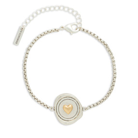 A silver metal bracelet that has a round mixed metal charm with a heart inside.