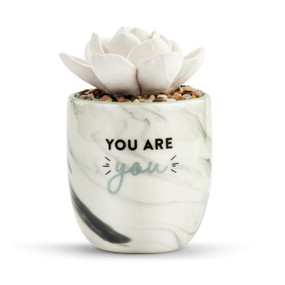 White and black marble planter that says "You are you" with a fake white succulent inside that works as a diffuser.