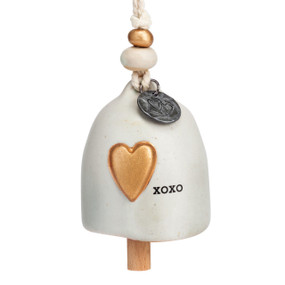 A mini cream bell that says "XOXO" and has a gold heart. There are beads and a metal token at the top of the bell.