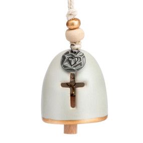 A mini cream bell with a cutout in the shape of a cross. There are beads and a metal token at the top of the bell.