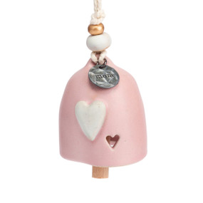 A mini pink bell with a white heart and small cutout heart. There are beads and a metal token at the top of the bell.