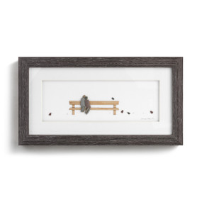 A rectangular dark wood framed wall art piece showing a couple sitting on a wood bench and small birds depicted with small stones.