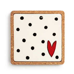 A square cork base holding a white stoneware trivet inside with black dots and a red heart.