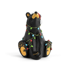 A sitting black bear figurine wearing a Santa hat and tangled up in a string of holiday lights.