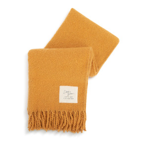 A light orange fringed blanket with a fabric patch in the lower right corner that says "Dear You, Take A Rest To Be Your Best".