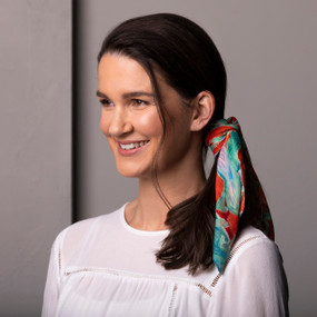 A smiling woman wearing a white blouse and has her hair tied in a ponytail with a red and green floral neckerchief with art inspired by ArtLifting artist Alicia Sterling Beach.