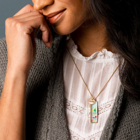A smiling woman wearing a vertical bar necklace with an image of a poppy field inspired by artwork created by ArtLifting artist Midori.