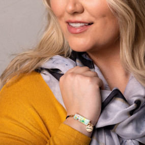 A blonde woman wearing a mustard colored top, black and white scarf and a horizontal bar bracelet with a poppy field image inspired by artwork created by ArtLifting artist Midori.