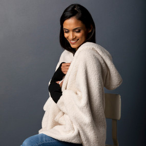 A sitting woman wearing a cream Sherpa hooded wrap with black cuffs.
