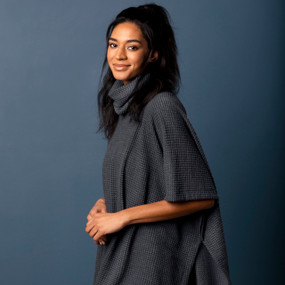 Side view of a smiling woman wearing a short sleeve charcoal colored waffle knit poncho.