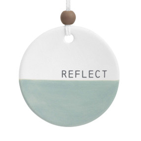 A round ceramic hanging diffuser that says "Reflect" in the white half and the other half is green.