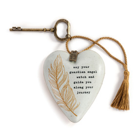 A heart shaped sculpture with a gold key and gold tassel that has a gold feather and a saying about your guardian angel.