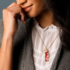 A smiling woman wearing a vertical bar necklace with an image of florals on a red background inspired by artwork created by ArtLifting artist Alicia Sterling Beach.