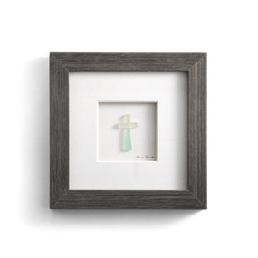 A gray wood framed image of a cross made of light stone pebbles.