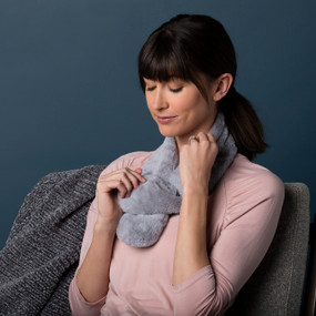 A woman wearing a pink top and a soft gray warming scarf around her neck.