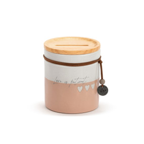 A peach and white round ceramic container that says "Love is Patient". The container has a wood lid with an open slot and a leather cord around the jar with a metal token that says "XOXO".