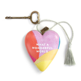 A heart shaped sculpture with a gold key and silver tassel featuring artwork created by ArtLifting artist Christina Constantine. The image is purple, yellow and orange colors  and says "What A Wonderful World".