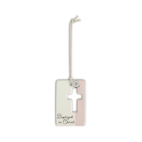 A pink and cream hanging token with a cross cutout and round silver charm with a heart attached to the hanger. The bottom of the token says "Baptized in Christ".