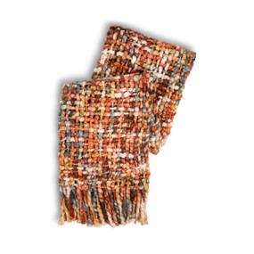 A woven fringed blanket with warm red, orange and cream colors, displayed folded on itself.