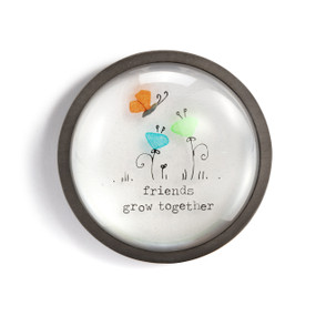 A round paperweight with a wood frame and the image of a butterfly and flowers that says "friends grow together".