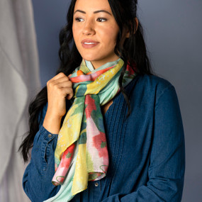 A woman in a denim top wearing a rectangular scarf with a pink and green floral pattern with artwork inspired by ArtLifting artist Midori, around her neck.
