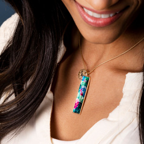 Close up of a woman wearing a vertical bar necklace with an image of pink, blue and green hydrangea inspired by artwork created by ArtLifting artist Midori.