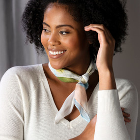 A smiling woman wearing a neckerchief tied around her neck with artwork inspired by ArtLifting artist Charlie French that has bold paint squares in blue and green on a light background.