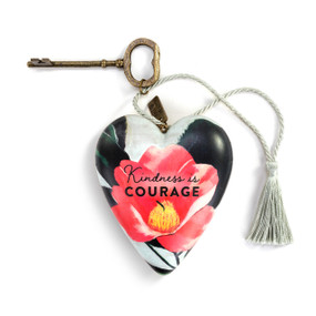 A heart shaped sculpture with a gold key and silver tassel featuring artwork created by ArtLifting artist Midori. The image is a pink camellia flower and says "Kindness is Courage".