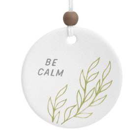 A round white ceramic hanging diffuser that says "Be Calm" with line drawn green leaves.