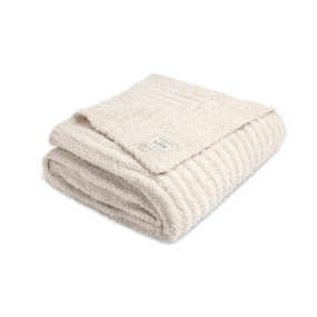 A cream ribbed blanket with a fabric patch on the corner, displayed folded on a white background.