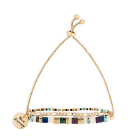 A gold chain adjustable bracelet with beads and tiles in gold green and white. The bracelet also has a gold round charm that says New Journey.