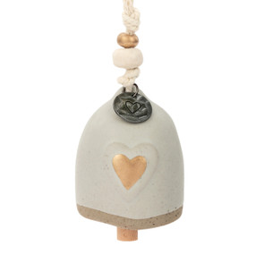 A cream bell with decorative beads and metal token. There is a gold heart on the front.
