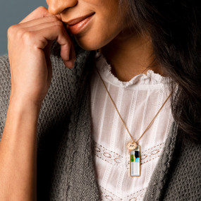 A smiling woman wearing a vertical bar necklace with an image inspired by artwork created by ArtLifting artist Charlie French of squares of blue and green.