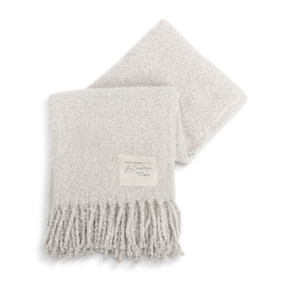 A light gray fringed blanket with a fabric patch in the lower right corner that says "Wrap Yourself in Blessings and Be At Peace".