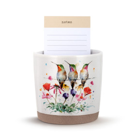 A white stoneware planter with a watercolor image of hummingbirds on a wire above wildflowers. The planter has a tan textured base and a lined notepad inside.