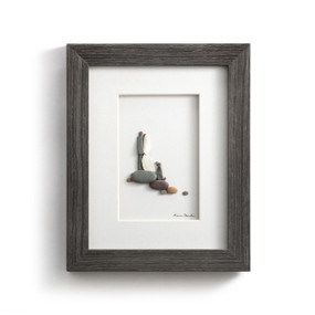 A gray wood framed image of a wedding couple and their dog made of pebbles.