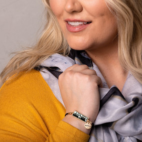 A blonde woman wearing a mustard colored top, black and white scarf and a horizontal bar bracelet with a black and white pattern image inspired by artwork created by ArtLifting artist Linda King.