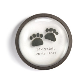 A round paperweight with a wood frame and the image of two paw prints made of pebbles and that says "paw prints on my heart".