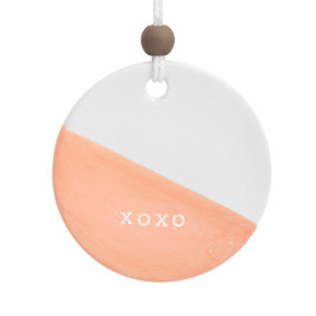 A round peach and white ceramic hanging diffuser that says "XOXO" in the peach portion of the diffuser.