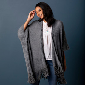Front facing view of a smiling woman wearing a charcoal colored textured duster, a white shirt and jeans.